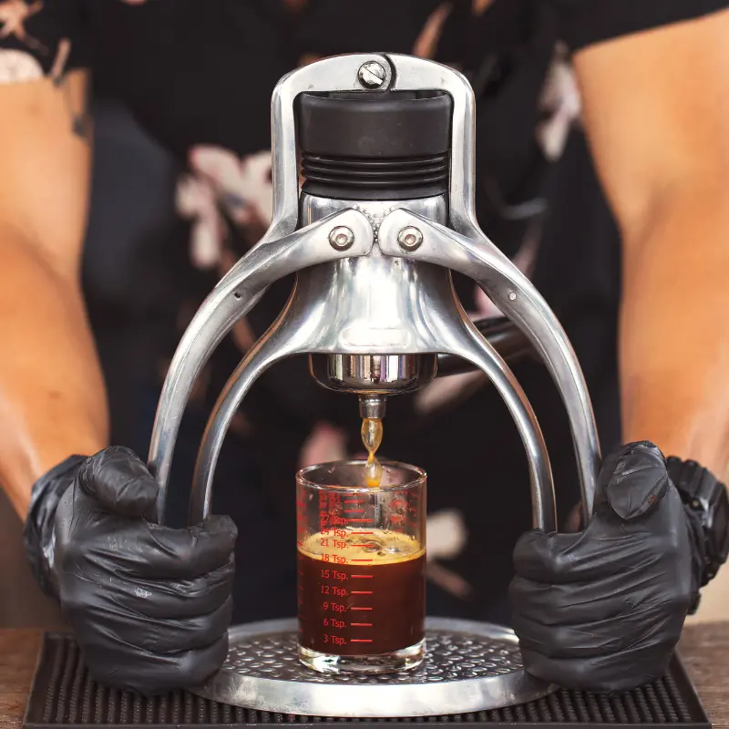 Man pressing down on his manual espresso maker and espresso being squeezed out of it