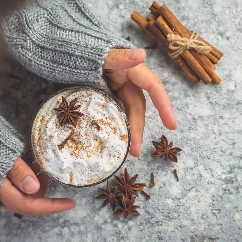 hands holding a cup of Chai Coffee‍ with cinnamon sticks